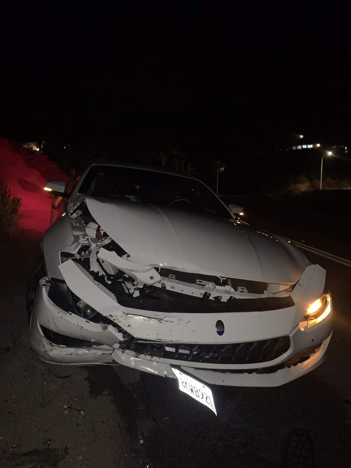 The totaled white Maserati with a crushed front end after a night crash