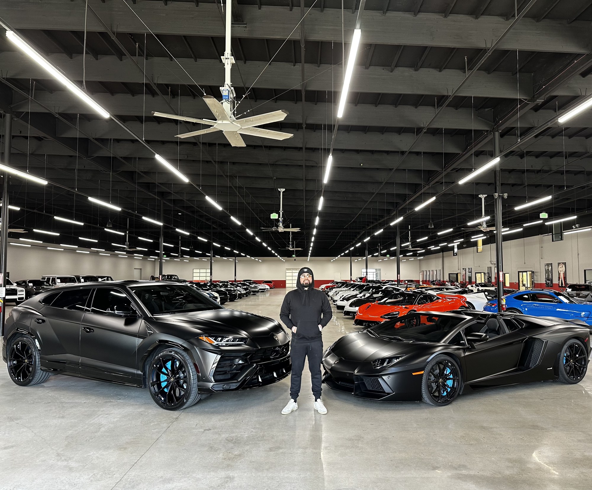 Coach P standing between his Lamborghini Urus and Aventador in a warehouse